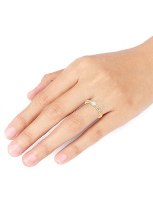 Guldring med en glat ring med en central mintgrøn sten og tre små klare sten på den ene side; båret på en hånd med naturlige negle.
