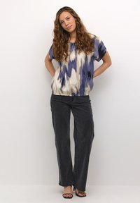 Multicolored short-sleeve top with blue, cream, and black abstract patterns; paired with high-waisted dark jeans and black heeled sandals.