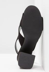 Sandale noire à talon avec semelle texturée et talon bloc, vue par dessous sur fond blanc.