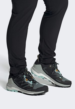 Chaussures de randonnée noires et grises avec une tige en mesh texturé, semelle en caoutchouc et accents turquoise. Présente des lacets à motif et un talon renforcé.