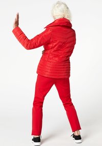 Röd vadderad jacka med hög krage, horisontell sömnad och vinklad design. Matchad med röda byxor och svarta sneakers.