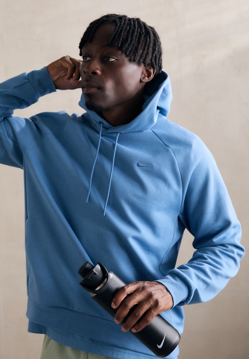 Blue hoodie with a drawstring and kangaroo pocket, made of smooth fabric. Holding a black water bottle with a logo.