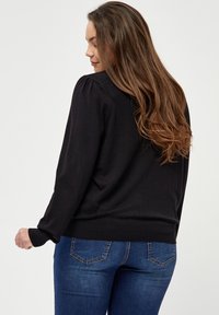 Czarny sweter z długim rękawem, z prążkowanymi mankietami i dolnym brzegiem. W połączeniu z dopasowanymi niebieskimi dżinsami. Gładka tekstura, prosty design.