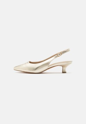 Chaussure slingback dorée à bout pointu, petit talon kitten et bride réglable avec boucle sur un fond blanc uni.