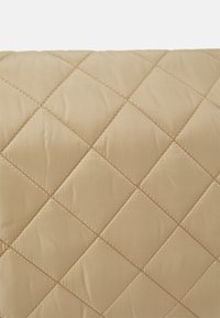 Tessuto beige trapuntato con motivo a diamante, caratterizzato da una texture liscia e outlines cuciti, adatto per biancheria da letto o tappezzeria.