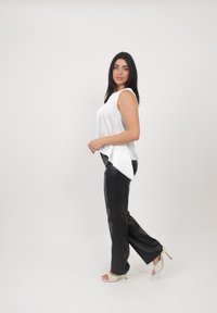 Witte mouwloze top met een gebogen zoom, gecombineerd met zwarte neplederen wijde broek en witte sandaaltjes met hoge hakken.