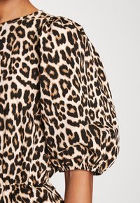 Leopardmönstrad topp med puffärmar, tillverkad av mjukt tyg med gulddetaljer och en figurnära midjedetalj. Basfärgen är ljusbeige.