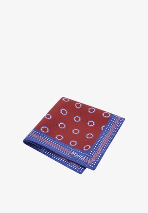 Złożona czerwona jedwabna chusteczka do kieszeni z niebieskimi i białymi okrągłymi wzorami oraz niebieską bordiurą z małymi białymi kropkami i czerwonymi kwadratami.