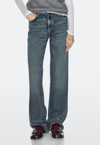 Wide-leg denim jeans in dark blue, featuring a classic five-pocket design and subtle fading. Paired with brown tassel loafers.