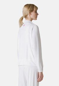 Sweatshirt blanc à manches longues et poignets élastiques, avec un détail logo rose à l'arrière. Texture douce, design simple et coupe ample.