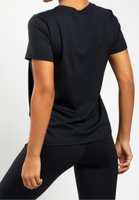 Černé tričko s krátkým rukávem vyrobené z hladké tkaniny, s volným střihem a kulatým výstřihem. Zadní strana má minimální švy a čistý vzhled.