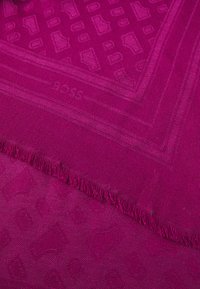 Tkana marama u vibrantnoj fuksiji, s reljefnim uzorkom geometrijskih oblika i resicama na rubovima za teksturu i detalj.