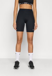 Μαύρα ποδηλατικά σορτς με ψηλή μέση και εφαρμοστή σχεδίαση με το λογότυπο της Nike. Συνδυασμένα με μαύρα αθλητικ ά παπούτσια και λευκές καλτσες crew με μαύρες λεπτομέρειες.