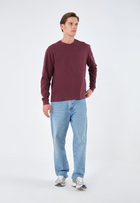 Burgunderfarbenes Langarmhemd, blaue Jeans und silberne Sneakers. Einfaches Design mit Rundhalsausschnitt und lässiger Passform.