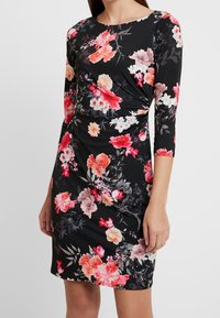 Zwarte bloemenjurk met driekwartmouwen, met een levendige mix van roze en witte bloemen op rekbare stof, met geraffineerde zijkantdetails.