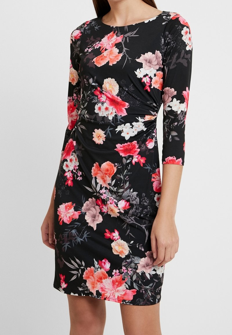 Czarna sukienka w kwiaty z trzema ćwierć rękawami, z żywym połączeniem różowych i białych kwiatów na elastycznym materiale, z marszczeniami po bokach.
