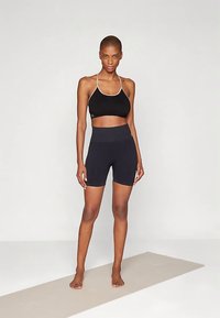 Juodas sportinis liemenėlė su plonais dirželiais ir elastine juosta; derančios tamsios aptemptos šortai. Lygus paviršius, paprastas dizainas ir prigludęs siluetas.