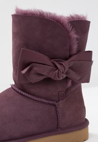 Botte d'hiver en daim violet avec doublure en fourrure douce et grand nœud en cuir sur le côté, dotée d'une semelle en caoutchouc plate marron.