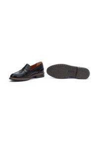 Mocassins en cuir noir avec une finition lisse, un talon plat et une sangle décorative. La semelle est en caoutchouc texturé pour une meilleure adhérence et durabilité.