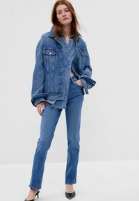 Denim oversized jakna svijetloplavog pranja, s kopčanjem na gumbi i prednjim džepovima, u kombinaciji s uskim svijetloplavim trapericama i crnim štiklama.