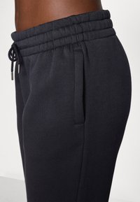 Čierne joggingové nohavice vyrobené z jemného, elastického materiálu. Majú elastický pás so šnúrkou a bočné vrecká. Skladaný strih.