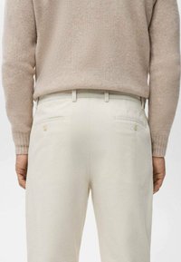 Pantalones de pana crema con un corte ajustado, que cuentan con bolsillos traseros y una textura sutil, combinados con un suéter de punto beige.