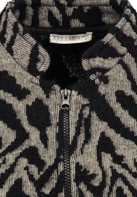 Primo piano di un maglione lavorato a maglia con stampa animale nera e beige, dotato di zip e etichetta del marchio Key Largo all'interno del colletto.