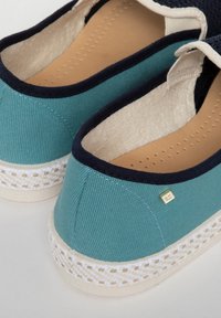Canvas espadrilles in teal en navy, met een textuur bovenkant, romige binnenzool en een geweven jute zool met een gouden logo-accent.