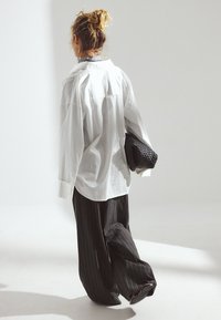 Ohlapna bela srajca in črne hlače s črtami. Obleka vključuje teksturirano črno pleteno torbico, ki poudarja kontrast in obliko.