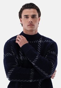 Dunkelblauer Pullover mit hohem Kragen, der ein graues geometrisches Muster und strukturierten Strickstoff aufweist. Gerippte Bündchen und Saum.