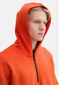 Sudadera con capucha naranja y cierre de cremallera en la parte delantera, con una suave tela de mezcla de algodón y un diseño casual.
