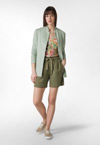 Ljusgrön jacka, färgglad mönstrad topp, olivgröna shorts och beige sneakers. Slät tyg, avslappnad passform och elastisk midja.