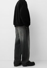 Svart fleecejacka med hög krage, parat med löst sittande mörkgrå jeans och svarta skor med tjock sula. Enkel design och texturer.