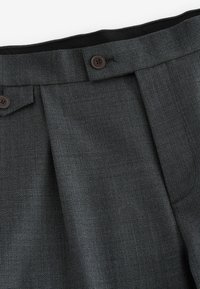 Pantalones grises con pliegues en un tejido texturizado, con dos botones marrones en la cintura y un forro interno negro suave.