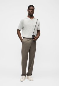 Ανοιχτό γκρι πλεκτό κοντομάνικο πόλο πουκάμισο, μπεζ παντελόνι καλοραμμένο, κρεμ αθλητικά παπούτσια και μικρή μαύρη τσάντα χιαστί. Απλός, μοντέρνος σχεδιασμός.