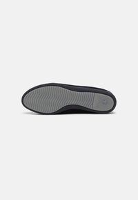 Semelle d'une chaussure noire avec une semelle en caoutchouc gris texturé présentant un motif ondulé et la pointure 37 près du talon.