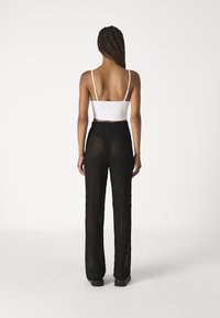 Czarne szerokie spodnie z koronki z fakturowanym wzorem, zestawione z dopasowanym białym topem na cienkich ramiączkach. Fason luźny.