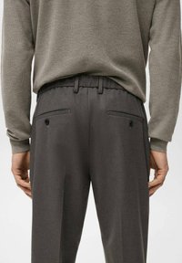 Temno sivi hlače z gladko teksturo, elastičnim pasom, dvema zadnjima žepoma s gumbi in prirejenim dizajnom. Vlečem jih z svetlo sivo majico.