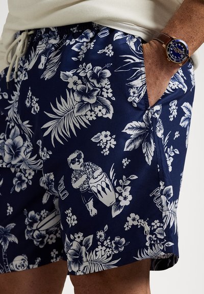 Tumši zilas peldbikses ar baltām ziedu un dzīvnieku apdrukām. Audums ir viegls, ar elastīgu jostu un auklu.