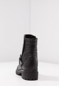 Bottines noires en cuir avec une texture matelassée, ornées de petits clous le long du bord supérieur, et avec un bout arrondi. Semelle en caoutchouc.