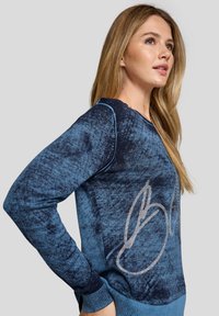 Blauer Pullover mit strukturiertem Design und dunkelblauen Akzenten, langen Ärmeln, rundem Halsausschnitt und einem glänzenden silbernen Logo-Detail.