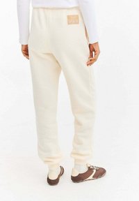 Kremowe spodnie dresowe o luźnym kroju, z elastycznym pasem, ściągaczami przy nogawkach oraz małą naszywką z logo na plecach.