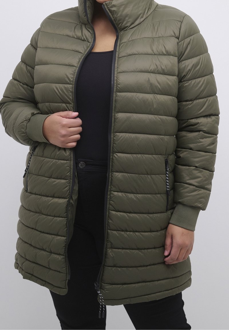 Oliivinvihreä toppatakki, jossa vaakasuuntaiset tikatut kuviot, korkea kaulus, vetoketju edessä ja sivutaskut, sekä resorireunukset ja teksturoitu kangas.