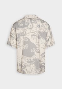 Camisa de manga corta en beige, con un diseño abstracto en gris apagado. Hecha de tejido ligero con cuello y corte holgado.