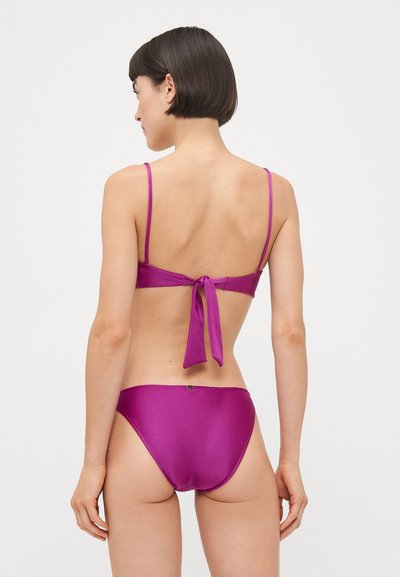 Violeta bikini komplekts ar satīna tekstūru, plānām siksniņām un saistāmu aizmuguri, ar zemu jostasvietu apakšdaļām un minimālistisku dizainu.
