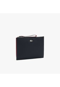 Pochette synthétique bleu marine avec un accent rouge. Fermeture éclair, bracelet de poignet, et petit logo argenté sur le devant. Texture lisse.