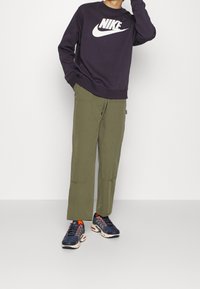 Dark purple sweatshirt with white Nike logo, paired with olive green pants. Footwear features dark blue design with orange accents.