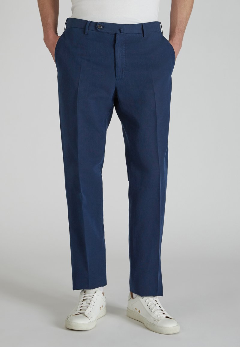 Granatowe spodnie o dopasowanym kroju, z przodem zapinanym na guzik, bocznymi kieszeniami oraz gładkim, lekkim materiałem. Połączone z białymi sneakersami.