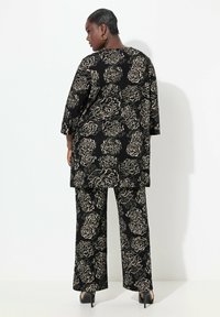 Mustakukkainen asu, jossa on pitkä paita kolmneljänneksen hihoilla ja leveät housut, molemmissa teksturoitu pinta ja kultaiset yksityiskohdat.