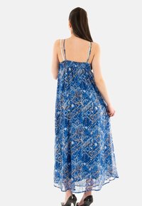 Abito lungo blu con motivi intricati; tessuto leggero, spalline regolabili, silhouette fluente e una texture leggermente trasparente.